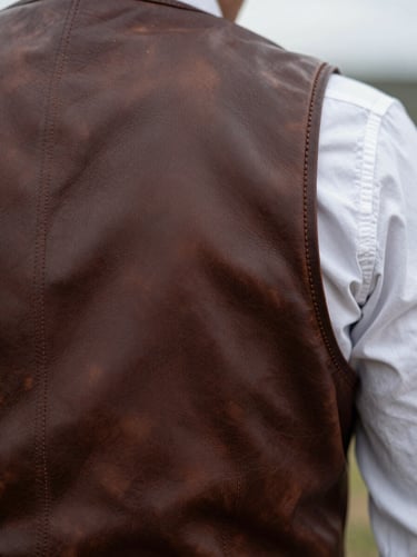 Close-up of hand-burnished leather edges on a bespoke western vest, raw texture, overcast daylight
