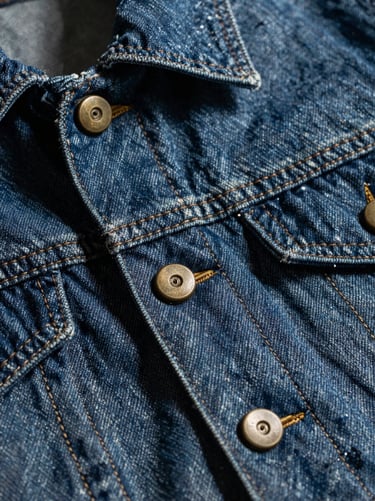 Extreme macro detail of heavy-gauge stitching on a raw denim jacket, bronze hardware, dramatic shadows