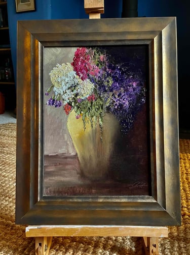 Impasto oil painting of colorful flowers in a yellow vase, displayed in a bronze frame on a wooden easel.