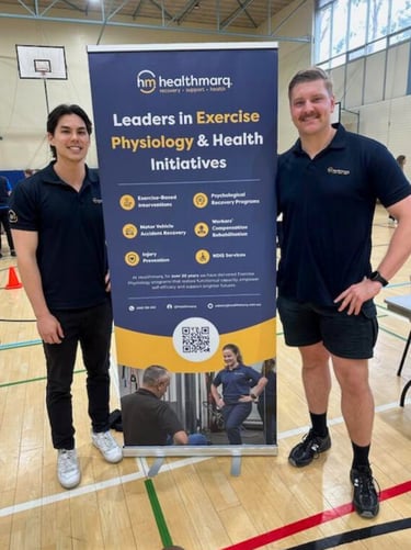 Healthmarq exercise physiology specialists standing with a promotional banner inside a fitness gymnasium.