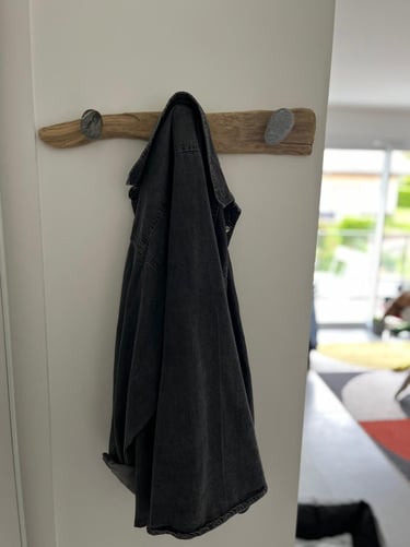 Rustic driftwood wall coat rack with smooth pebble hooks holding a black denim jacket.