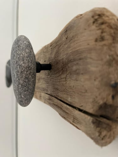 Rustic coat rack made of natural driftwood with smooth grey stone wall hooks.