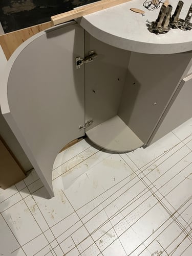 Modern curved light grey kitchen cabinet with an open door showing interior hinges and stone countertop.