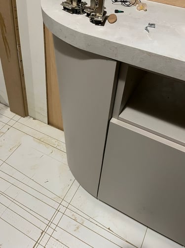 Modern curved light grey kitchen cabinet with a stone countertop during installation.