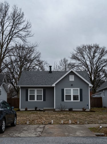 Overcast exterior of a small house, a car in the driveway, bare winter trees, flat digital gray, no filters