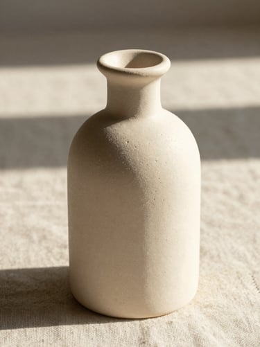 Macro photograph of a textured cream ceramic bottle on a heavy linen surface, soft morning light, warm shadows.