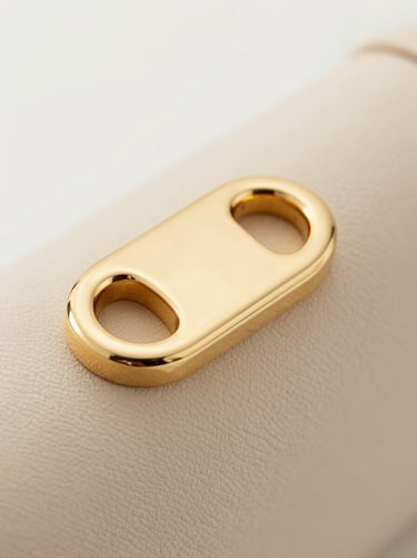 Macro detail of custom gold-plated metal hardware on structured beige leather, soft diffused studio light.
