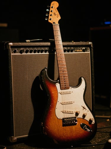 Gritty close-up of a well-worn electric guitar resting against a vintage tube amplifier on a dark stage, warm tungsten glow, 35mm film grain.