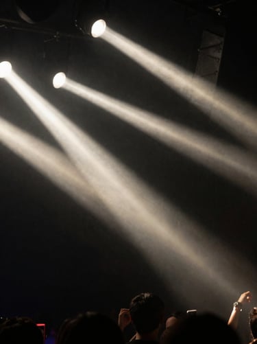 A blurry, artistic shot of stage lights through a hazy rock club atmosphere. High contrast with deep black and soft off-white streaks.