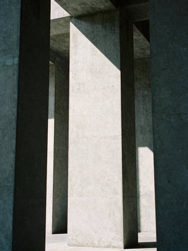 Abstract geometric composition of concrete pillars under harsh overhead light, stark contrast, desaturated cool tones, 35mm film grain.