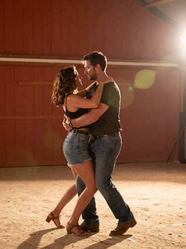 A candid moment of a couple dancing in a North American / US barn setting. The image is cinematic with warm lens flares and a color palette of soft sand and terracotta clay orange.