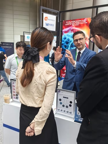 A biotech representative in a suit presents human cell research at a professional medical conference exhibit.