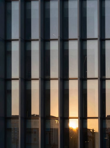 Abstract architectural shot of modern glass panels refracting warm sunlight into subtle rainbow spectrums, clean lines, dark background.
