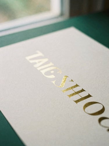 Macro shot of heavy artisanal paper with embossed gold foil typography, soft window light, deep forest green accents, 35mm film