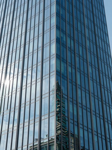 Close-up architectural detail of a modern glass skyscraper facade reflecting the blue sky, clean geometric lines.