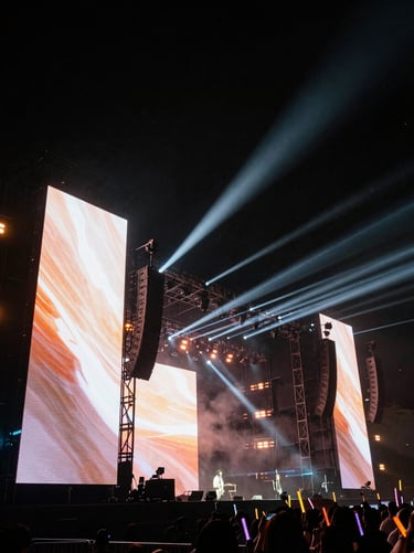 Massive live event stage, towering LED screens, dramatic laser beams piercing through haze, low-angle wide shot, high-contrast.