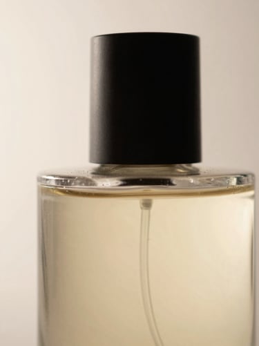 Extreme close-up of a cylindrical perfume bottle, raking light from the left revealing the curve of the glass and the texture of the cap, matte surface, no warmth, pale background