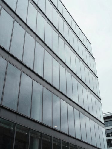 Crisp wide perspective of a modern office building facade, clean glass panels reflecting a gray sky, overcast daylight, 35mm.
