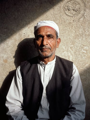 Portrait of a Pathan scholar in Quetta, wearing a traditional dark vest, dramatic natural shadows, thoughtful expression, 35mm documentary photography.
