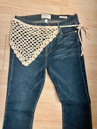 Pair of jeans laid out with crochet bandana belt wrapped around waist