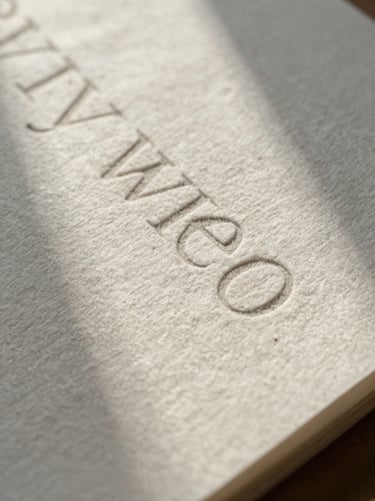 Extreme close-up of textured heavy-weight cotton paper packaging, debossed serif typography, soft overcast daylight shadow.