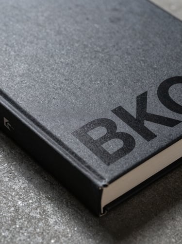 Extreme close-up of a textured matte book cover with bold technical typography, sharp shadows, resting on a dark concrete surface.