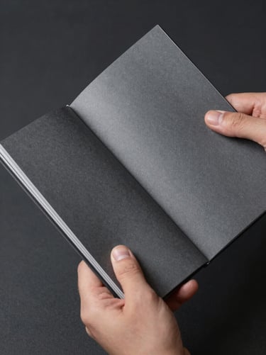 Close-up of hands holding a thick, matte-finished brand manual with silver foil details, shot in a desaturated, high-craft aesthetic against a deep charcoal background.