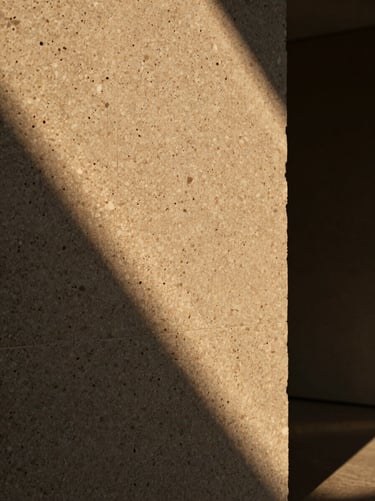 Cinematic close-up of textured travertine stone under low-angle golden light, deep shadows casting dramatic lines across the material, warm and sophisticated atmosphere.