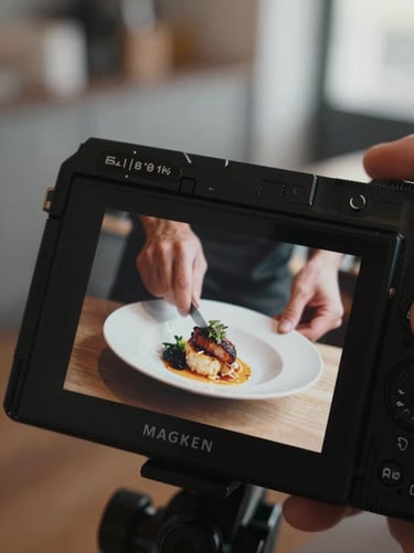 Close-up of a camera screen displaying a live food shoot, showing hands plating a dish in a quiet, Scandinavian-style restaurant kitchen, soft directional daylight, shallow depth of field.
