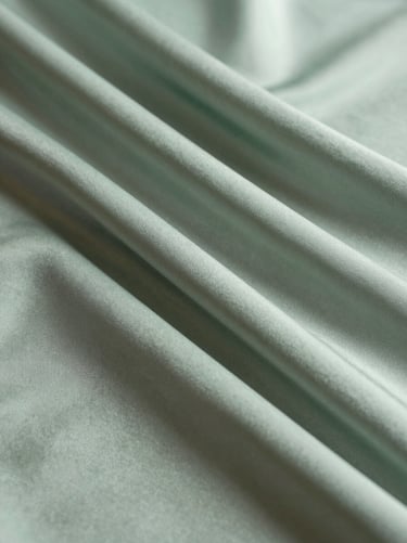 A detailed shot of layered fabric works. The overlapping silk creates new shades of muted sage green and pale silver-green, suggesting a deep, cosmic perspective within a confined space.
