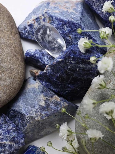 Cristales de sodalita azul en bruto y piedras de río lisas con flores blancas