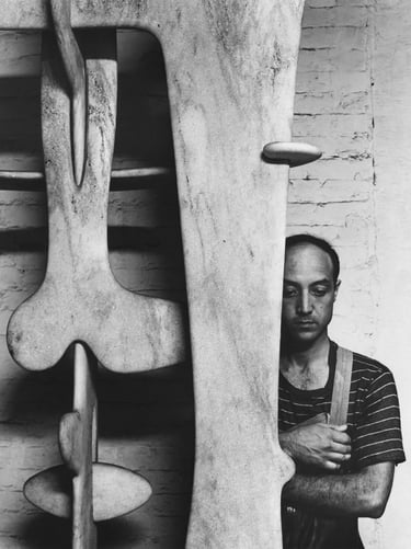 Black and white photograph of an artist beside a large abstract sculpture, showing the connection be