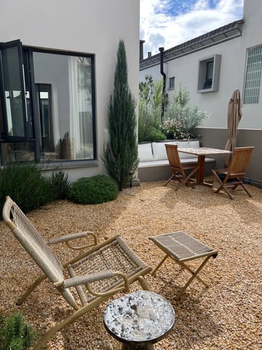 Quiet garden corner with gravel, wooden chairs, small table, white walls and simple planting for rel