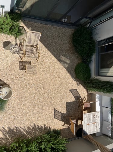 Minimal courtyard garden with gravel surface, simple outdoor chairs and small trees, creating a calm