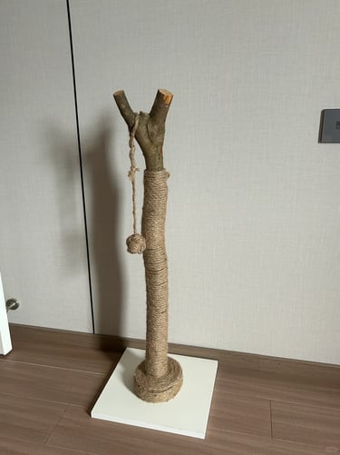 Natural branch-style sisal cat scratching post with a hanging toy on a white base in a simple home c
