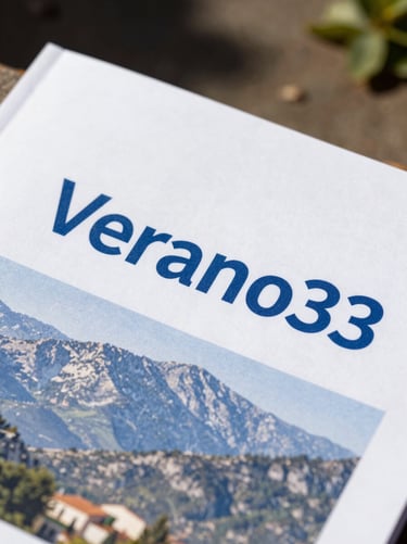 Close-up shot of a printed official document cover titled 'Verano' with blue corporate branding, outdoor setting with Guadarrama mountains blurred in the background, bright summer daylight.