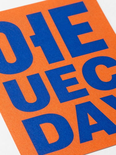 Extreme close-up of a bold graphic poster with heavy grotesque typography in electric blue on a vivid orange background, sharp paper texture