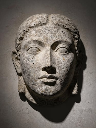 Frontal view of a textured basalt wall sculpture hanging on a raw plaster surface, dramatic chiaroscuro lighting