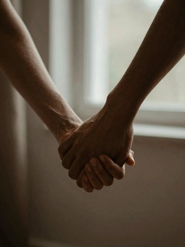 Close-up of hands holding hands in a supportive gesture, soft diffused window light, deep muted tones, warm editorial photography, 35mm lens