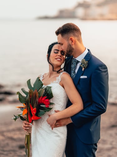 una novia y un novio en una playa abrazándose en el día de su boda