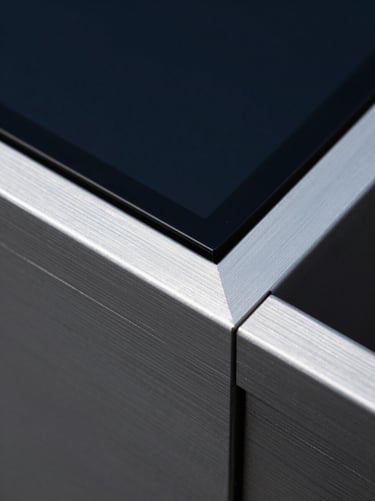 Macro shot of physical brushed aluminum and dark glass with razor-sharp geometric cuts, low-key cool silver highlights, deep indigo shadows.