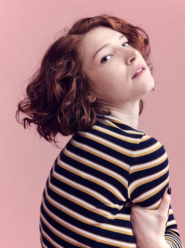 Ein Kopfbild einer jungen Frau mit roten Haaren und gestreiftem Hemd.