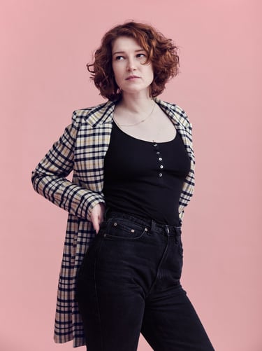 A young woman with red hair standing in front of a pink background.
