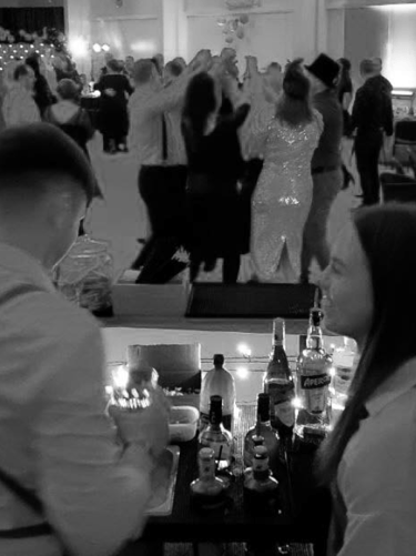 Bartenders serving guests at a crowded wedding reception event in black and white.