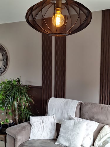 Un luminaire allumé en tissu noir devant un mur beige et des panneaux décoratifs bruns