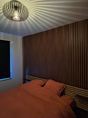 Lit terracotta avec panneau en latte de bois clair et foncé servant de tête de lit et luminaire noir