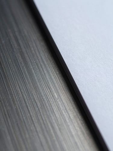 Extreme close-up macro shot of brushed metal intersecting with heavy matte paper, cool diffused studio lighting, sharp focus.
