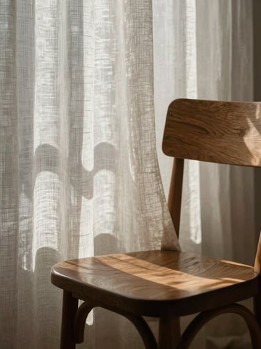 A poetic and artistic close-up of light filtering through a sheer, textured linen curtain, casting delicate and abstract geometric shadows onto a beautifully designed wooden chair. The image feels deeply quiet, high-fashion, and sophisticated.