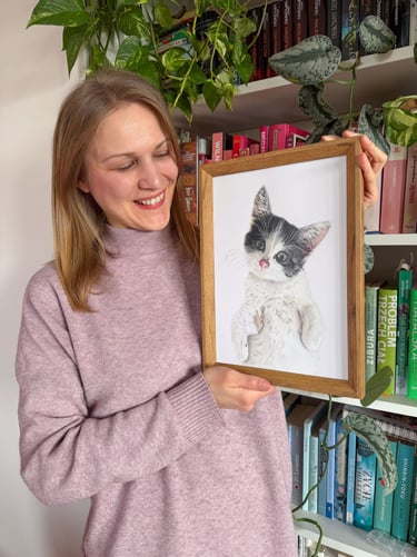 Pet portrait artist holing a framed colored pencil custom drawing of a black and white kitten