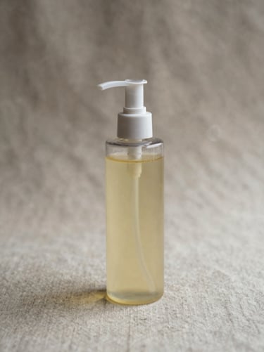 A minimalist glass bottle of oil cleanser with a clear pump, resting on a raw linen background, soft side lighting, portrait aspect.